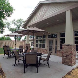 A cozy outdoor patio with tables and chairs under umbrellas, set in a backyard.