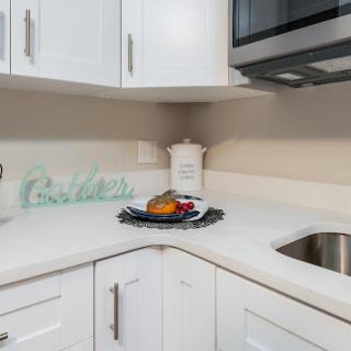 A sleek and modern kitchen corner featuring white cabinets, a countertop adorned with a bowl of fruit, and essential appliances.