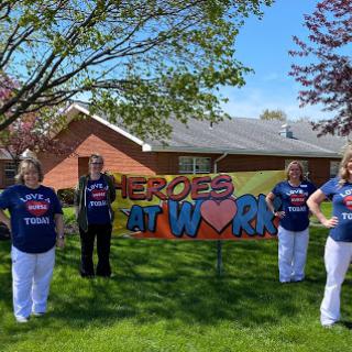 A group of individuals proudly displaying a sign that reads 'Heroes at Work', celebrating dedication and teamwork in a vibrant outdoor setting.