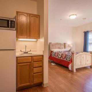 A cozy studio apartment featuring a compact kitchen and a bedroom area with wooden furniture.