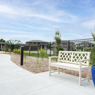 A white bench placed alongside a garden pathway with surrounding greenery and a black metal fence.