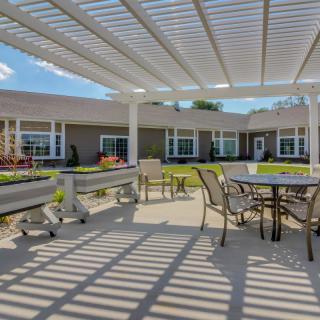 A sunny outdoor patio with a pergola, featuring tables and chairs for seating.