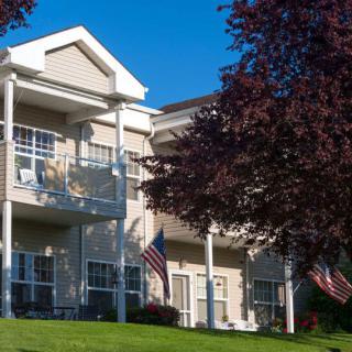 A residential apartment building with balconies, surrounded by trees and featuring American flags against a clear blue sky.