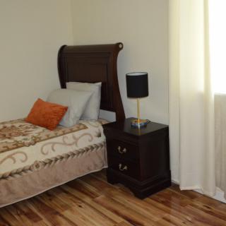 A cozy bedroom with a single bed, nightstand, and lamp by the window.