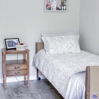 A minimalist bedroom with a single bed and a wooden nightstand, decorated with a framed photo and other small items.