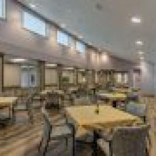 A spacious dining area with multiple tables and chairs, featuring modern lighting and high windows.