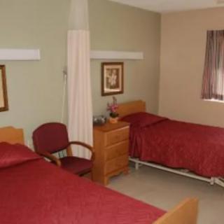 A hospital room featuring two twin beds with red bedspreads and a small dresser between them.