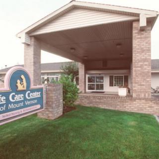 The image shows a building entrance with a sign and a well-maintained lawn.