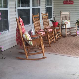 A cozy porch with several wooden rocking chairs and colorful cushions, perfect for relaxing.