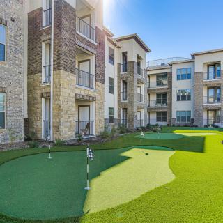 An apartment complex featuring a landscaped outdoor area with a putting green on a sunny day.