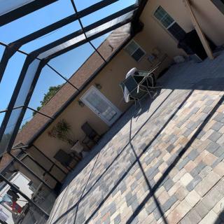 A sunny outdoor patio with pavers and a screened enclosure.