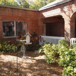 A peaceful courtyard with a brick building, featuring shrubs and a birdhouse.