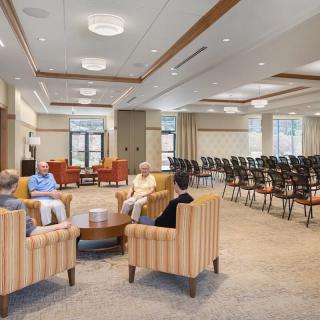 A modern conference room with a lounge area where people are sitting and conversing, surrounded by rows of chairs for additional seating.