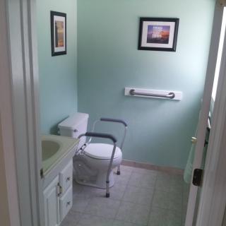 An accessible bathroom featuring a toilet with support rails and a small sink.