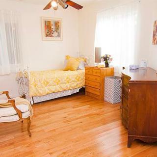 A cozy bedroom with wooden floors, featuring a single bed adorned with yellow bedding and decorative pillows.