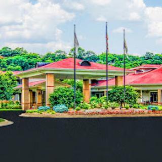 A welcoming hotel entrance surrounded by lush greenery and flagpoles against a picturesque sky.