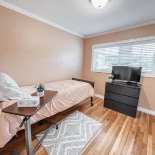 A minimalist bedroom with a single bed, dresser, and window, featuring neutral tones and hardwood flooring.