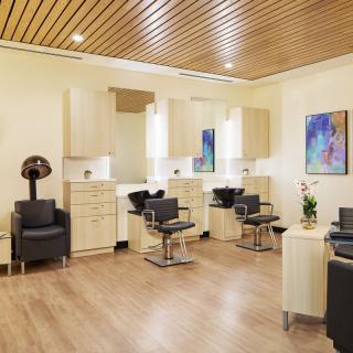 A modern hair salon with stylish chairs and mirrors, featuring wooden ceilings and contemporary artwork.