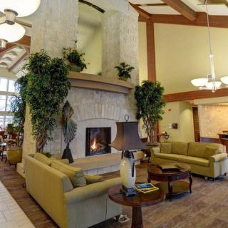 A cozy lobby interior featuring a central fireplace surrounded by comfortable sofas and decorative plants.
