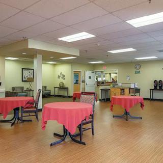 A well-lit cafeteria with round tables covered in red tablecloths, providing a welcoming community dining area.