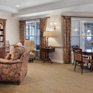 A cozy living room with a sofa, bookshelf, and a table with chairs near large windows.