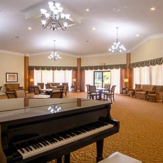 A spacious lounge area featuring a grand piano, elegant chandeliers, and comfortable seating.