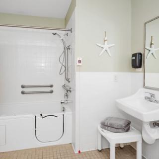 An accessible bathroom with a bathtub featuring support bars, a sink with a towel on a stool, and starfish-themed wall decor.