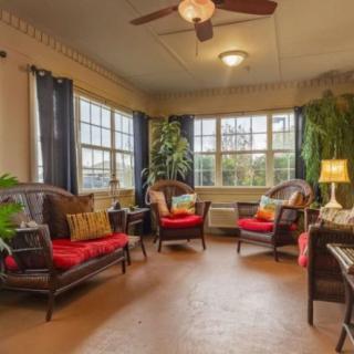 A cozy living room with wicker furniture, bright red cushions, and large windows allowing natural light to flood the space.