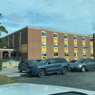 A view of a brick building with yellow accents and parked cars in the foreground.