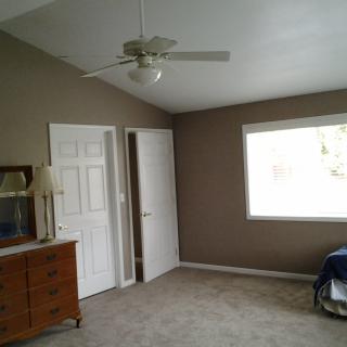 A neatly arranged bedroom with a dresser, lamp, ceiling fan, and window.