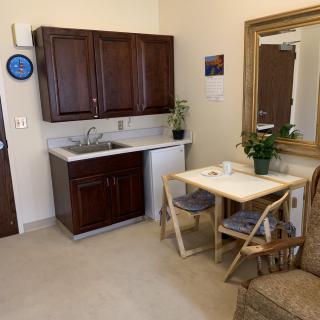 A cozy kitchenette featuring dark wood cabinets, a small table with chairs, and decorative plants.