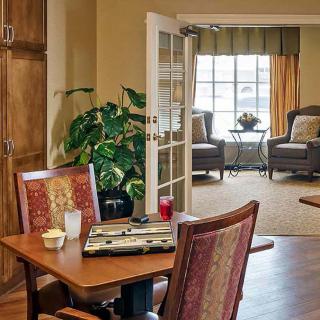 A cozy living room with comfortable seating, a table set for backgammon, and natural light streaming through the window.