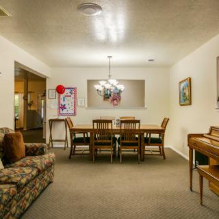 A cozy living and dining area featuring a wooden dining table set, an armchair, a piano, and decorative wall art.