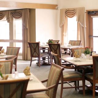 A cozy dining area with elegantly set tables and chairs, featuring soft natural light and decorative curtains.