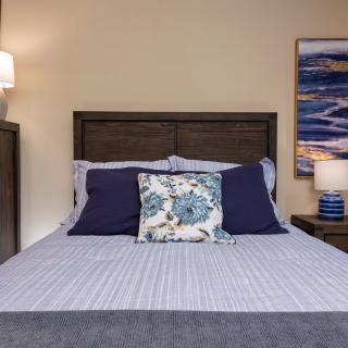 A neatly made bed with decorative pillows in a cozy bedroom, featuring a nightstand and a wall painting.