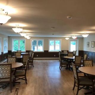A spacious dining room with multiple tables and chairs, featuring warm lighting and large windows.