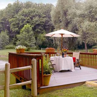 A peaceful outdoor deck with a table set under an umbrella, surrounded by lush greenery.