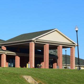 A brick building with columns and a sloped roof, set against a clear blue sky and surrounded by a green lawn.