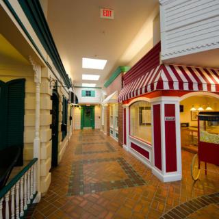 A vintage-style indoor hallway featuring storefronts with red and white awnings.