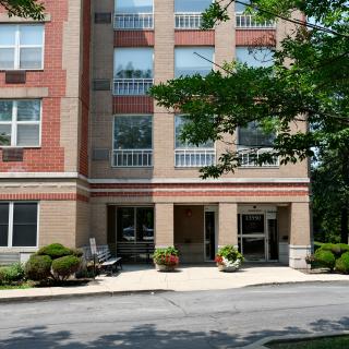 Front view of a residential building with an entrance surrounded by trees and sidewalk.