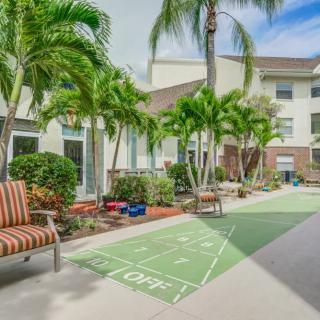 A tranquil courtyard featuring palm trees, a shuffleboard court, and comfortable outdoor seating next to a residential building.