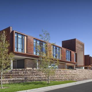 A modern school building with a brick facade and large windows under a clear blue sky.