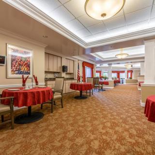 A spacious dining room with tables and chairs, adorned with red tablecloths and modern lighting.