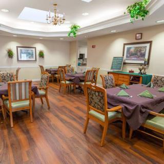 A well-decorated dining room with neatly arranged tables and chairs, featuring wood flooring and tasteful lighting.