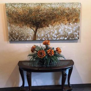 A decorative table with a floral arrangement sits beneath a painting of a tree.