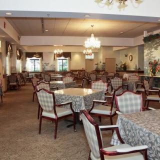An elegant dining room featuring multiple tables and chairs, lit by chandeliers.
