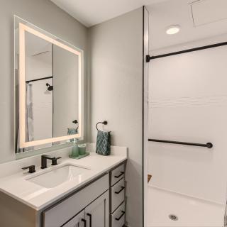 A modern bathroom featuring a sleek sink and illuminated mirror alongside a walk-in shower.