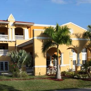 A tropical-style yellow house surrounded by palm trees and lush landscaping.