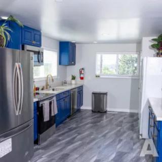A modern kitchen with blue cabinets, stainless steel appliances, and laminate flooring.