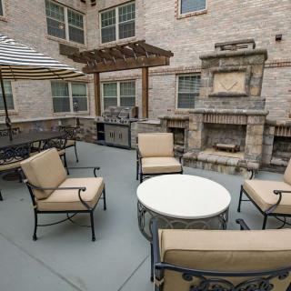An outdoor patio with a seating area, featuring cushioned chairs, a round table, and a built-in fireplace.